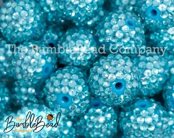 May include: Close-up of turquoise blue round beads covered in small clear rhinestones. The beads are arranged in a random pattern, creating a sparkling and eye-catching display.
