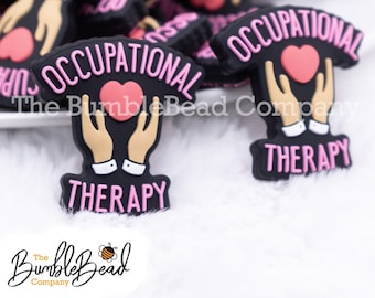 May include: Black and pink Occupational Therapy charms. The charms feature a heart held by hands, with the words "Occupational Therapy" and the BumbleBead Company logo. These charms are likely for crafting or jewelry making.