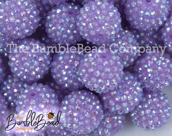 May include: A close-up of a pile of lavender-colored, round,  rhinestone-covered beads. The beads are shiny and have a light iridescent finish.