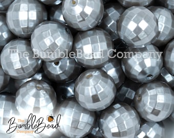 May include: A close-up of a pile of silver faceted round beads. The beads have a shiny, pearlescent finish.