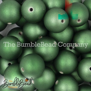 May include: A close-up of a pile of green, round, matte finish wooden beads. The beads have a hole in the center for stringing.
