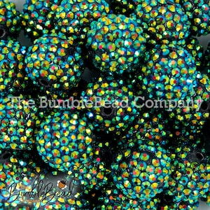 May include: A close-up of a pile of black round beads with iridescent green, blue, and red rhinestones. The beads are all the same size and are arranged in a random pattern. The beads are shiny and reflect light.