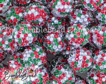 May include: Close-up of a group of red, green, and clear sparkly beads. The beads are all round and have a smooth, shiny finish. The beads are perfect for making jewelry or other crafts.