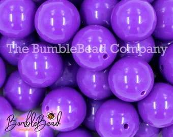 May include: A collection of glossy, round, purple beads with a hole drilled through each. The beads are scattered, filling the frame. The text "The BumbleBead Company" is visible in the image.