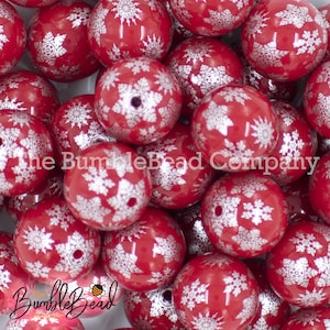 May include: A collection of red, round beads with a glossy finish. Each bead is decorated with a white snowflake pattern. The beads are from The BumbleBead Company.