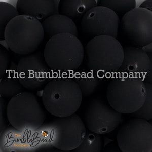 May include: A close-up image of a pile of black matte round beads. The beads are smooth and have a hole in the center. The beads are all the same size and are arranged in a random pattern. The text "The BumbleBead Company" is visible in the image.