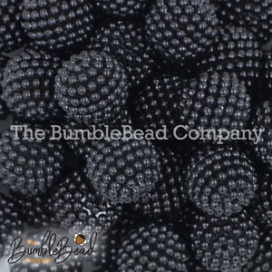 May include: A close-up image of a large quantity of black, round, textured beads. The beads have a bumpy, bubble-like surface. The beads are arranged in a random pattern, creating a visually interesting texture.