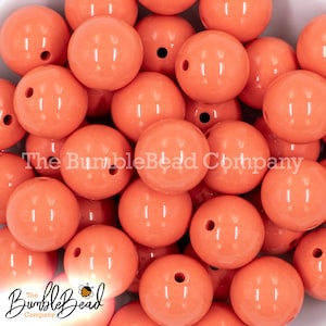 May include: A large pile of coral orange round beads. The beads are smooth and glossy.