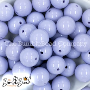 May include: A close-up of a pile of lavender-colored, round, plastic beads. The beads are smooth and shiny, and they have a small hole in the center.