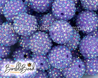 May include: A close-up of a group of purple iridescent round beads. The beads are covered in small, sparkly rhinestones.