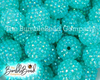 May include: A close-up image of a large quantity of turquoise blue round beads. The beads are covered in small, clear rhinestones, giving them a sparkly appearance. The beads are perfect for jewelry making, crafts, and home decor.