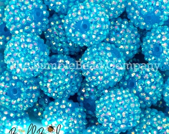 May include: A close-up of a pile of turquoise blue round beads covered in iridescent rhinestones. The beads are approximately 1 inch in diameter.