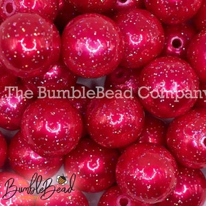 May include: A close-up of a pile of large, round, pink beads with a glittery finish. The beads are arranged in a random pattern and are all the same size. The beads are a bright, vibrant pink color and have a shiny, iridescent finish.