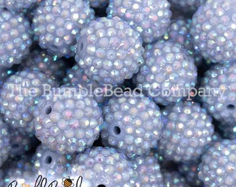 May include: A close-up of a pile of light blue iridescent round beads. The beads are covered in small, sparkly rhinestones.