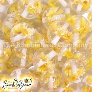 May include: Close-up of a group of clear round beads with yellow flowers and white accents inside. The beads are arranged in a random pattern. The text "The Bumble Bead Company" is visible in the background.
