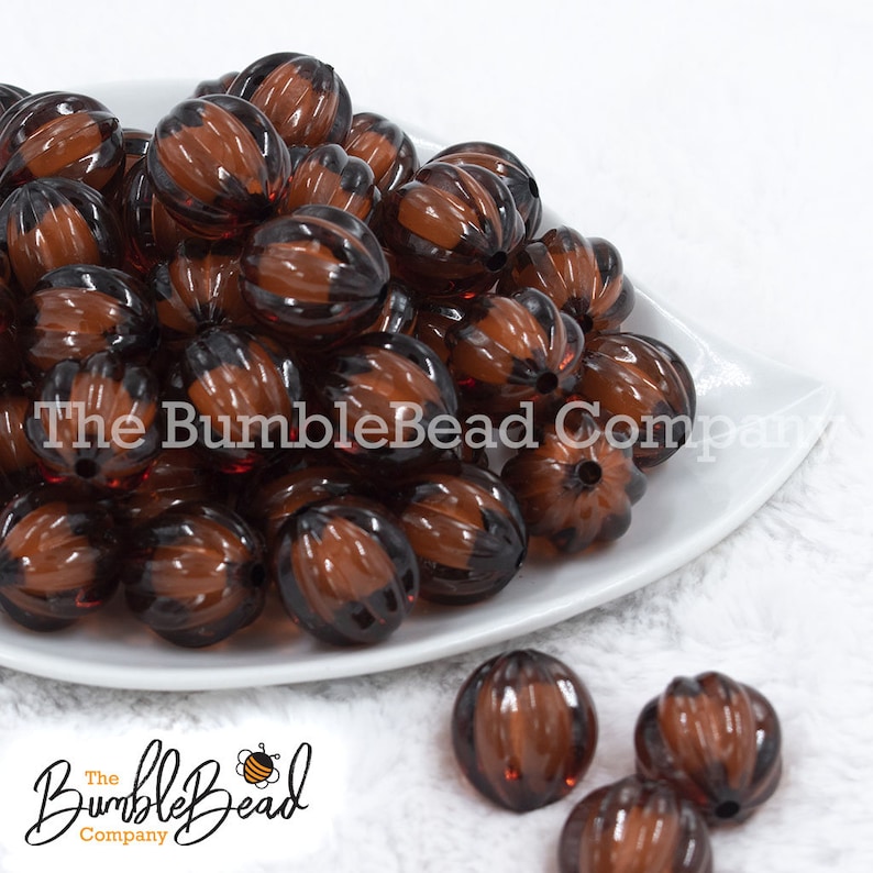 May include: A collection of brown and black ribbed beads, displayed on a white plate. The beads have a pumpkin-like shape and are translucent. The BumbleBead Company logo is visible in the image.