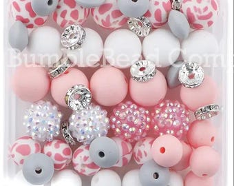 May include: A clear plastic container filled with a variety of colorful beads. The beads are pink, white, gray, and have a sparkly finish. Some beads have a patterned design. The container is labeled "Bumble Bead Com."