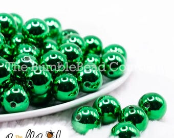 May include: Shiny, emerald green beads with a metallic finish are scattered on a white plate. The BumbleBead Company logo is visible in the lower left corner. These beads are perfect for jewelry making and crafting.