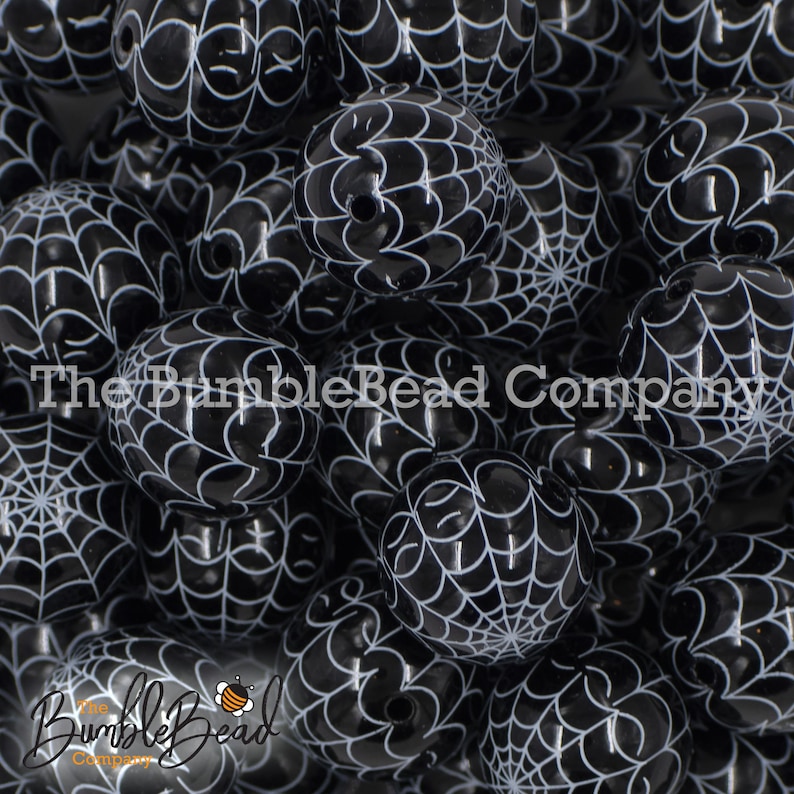 May include: A close-up of a pile of black and white spiderweb patterned beads. The beads are round and have a glossy finish.