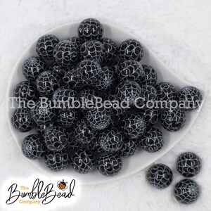 May include: A white bowl filled with black and white spiderweb patterned beads. The beads are round and have a glossy finish.