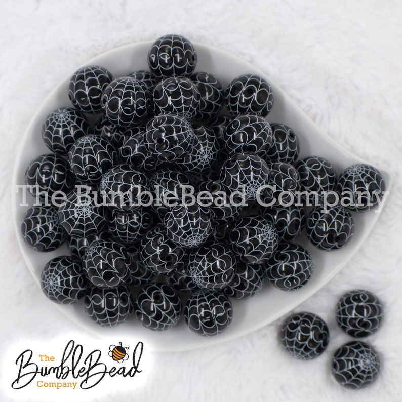 May include: A white bowl filled with black and white spiderweb patterned beads. The beads are round and have a glossy finish.