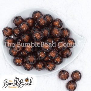 May include: A collection of brown and black striped beads in a white dish. The beads have a pumpkin shape with vertical grooves. The BumbleBead Company logo is visible in the image.