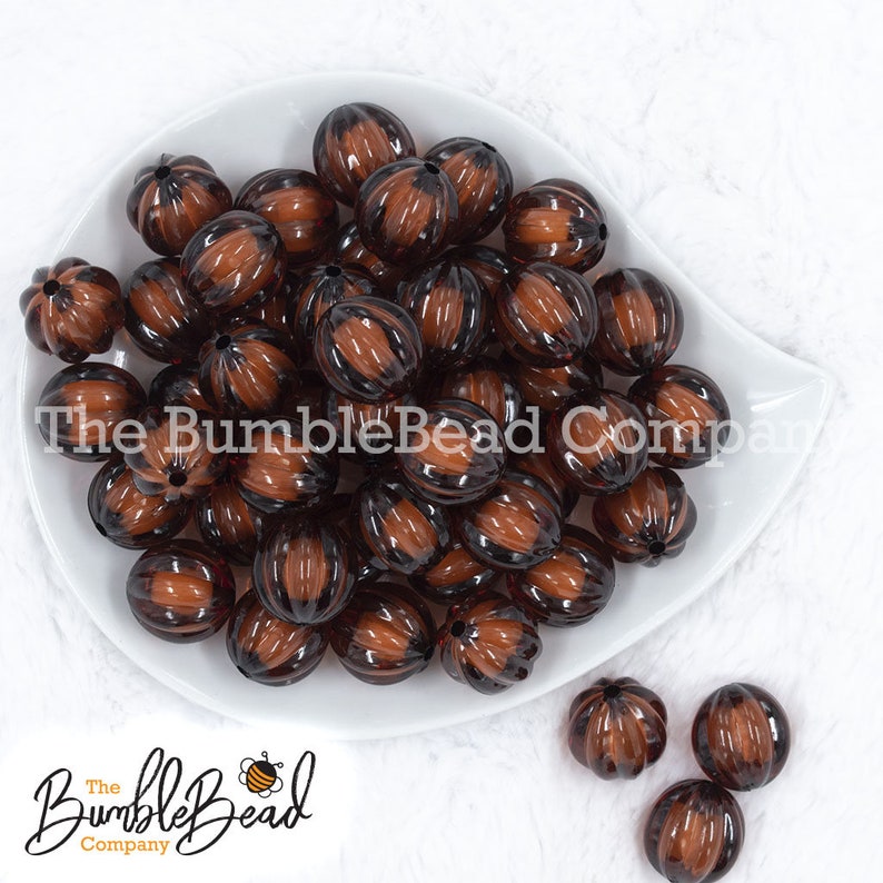 May include: A collection of brown and black striped beads in a white dish. The beads have a pumpkin shape with vertical grooves. The BumbleBead Company logo is visible in the image.
