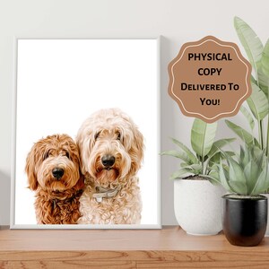 Op de afbeelding: Een ingelijste print met twee gekrulde honden, &eacute;&eacute;n roodbruin en de andere cr&egrave;mekleurig. De honden staan dicht bij elkaar en kijken de kijker aan. De print staat op een houten oppervlak, met planten op de achtergrond. De tekst op de afbeelding luidt "PHYSICAL COPY DELIVERED TO YOU!"