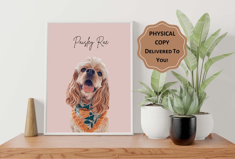 Op de afbeelding: Een ingelijst portret van een Cocker Spaniel-hond genaamd Paisley Rae, tegen een roze achtergrond. De hond heeft lichtbruine vacht, blauwe ogen en een bloemenbandana. De lijst bevat de tekst "Physical Copy Delivered to You!"