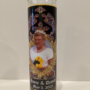 Op de afbeelding: Een witte glazen kaars met een zwart en gouden etiket. Het etiket toont een foto van een bruid die een boeket gele bloemen vasthoudt. De tekst op het etiket luidt "Joyce & David May 5, 2002".