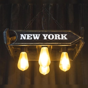May include: A wooden ceiling light fixture with a sign that reads "NEW YORK" and four Edison bulb lights.