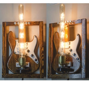 May include: Two wooden wall sconces shaped like electric guitars with clear glass bulbs. The sconces are painted in a dark brown wood grain finish.