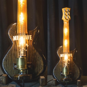 May include: A unique guitar-shaped lamp with a dark wood finish and a glowing Edison bulb. The lamp features the word "ME WAVE" in white lettering. The design incorporates a guitar body and neck, creating a striking decorative piece.