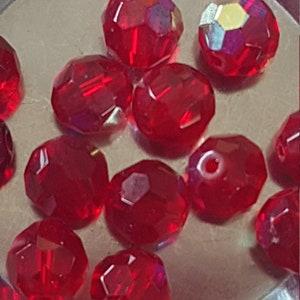 May include: A close-up of a group of red faceted glass beads. The beads are arranged in a random pattern on a silver surface.