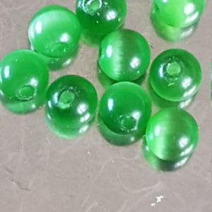 May include: A group of ten green glass beads with a hole in the center of each bead. The beads are round and have a smooth, shiny surface.
