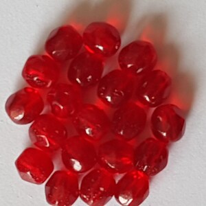 Puede incluir: Un montón de cuentas de vidrio rojas, cada una con una forma facetada ligeramente redondeada.