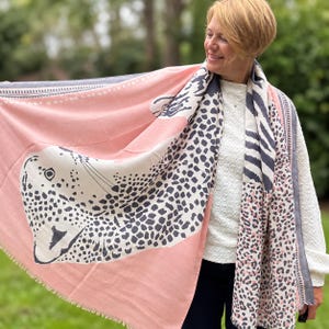 May include: A large rectangular scarf featuring a soft pink background with a prominent black and white leopard print graphic. The design includes sections of zebra stripes and smaller leopard spots, finished with a delicate fringed edge detail.