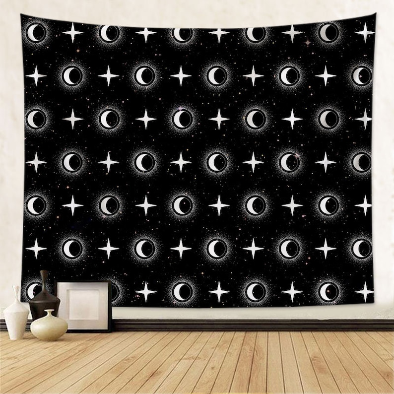 May include: Black tapestry with a repeating pattern of white crescent moons and stars. The tapestry is hanging on a wall with a wooden floor in front of it.