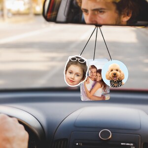 Puede incluir: Tres ambientadores de coche colgados de un espejo retrovisor. Los ambientadores est&aacute;n impresos con fotos de una ni&ntilde;a peque&ntilde;a con gafas de sol, una pareja y un perro.