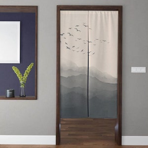 May include: A pair of beige room dividers with a mountain and bird design. The dividers are made of fabric and have a wood frame. The dividers are hanging on a wooden door frame.