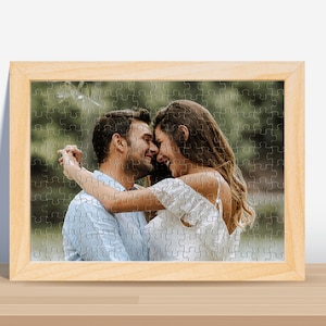 May include: A framed photograph of a couple embracing and looking at each other. The man is wearing a light blue shirt and the woman is wearing a white dress. The photo is set against a blurred background of green foliage.