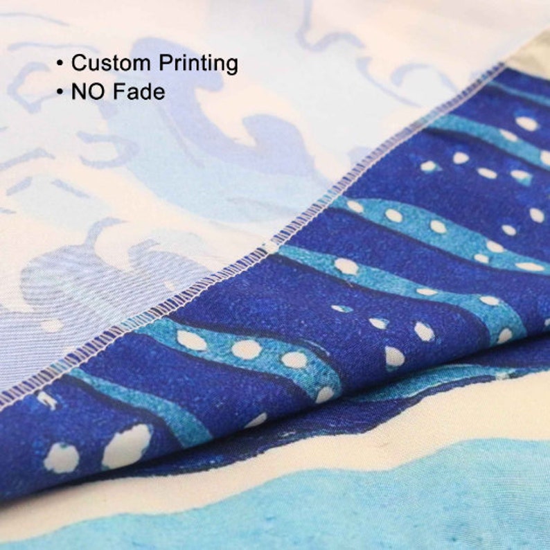 May include: Close-up of a fabric with a blue and white wave pattern. The fabric has the text "Custom Printing" and "NO Fade" printed on it. The fabric is folded, showing the edge with a stitched seam.