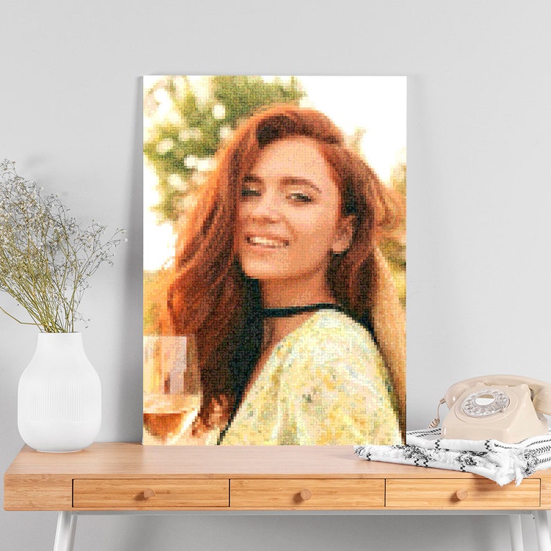 May include: A woman with long, red hair smiles while holding a glass of wine. She is wearing a floral patterned dress and is standing outdoors.