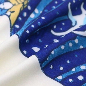 May include: Close-up of a fabric with a blue and white pattern. The design features curved lines, dots, and a stylized image, set against a white background. The fabric is folded, showing its texture and the interplay of colors.