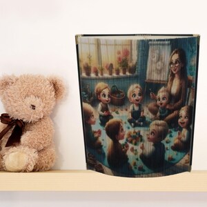Op de afbeelding: Een bruine teddybeer met een bruin lint zit naast een decoratief boek. Het boek toont een kleurrijke illustratie van een lerares die voorleest aan kinderen. De scène speelt zich af in een kamer met een raam en potplanten.