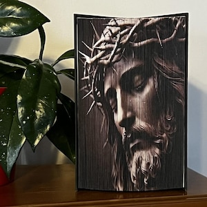 Può includere: Una scultura di arte di libro in bianco e nero di Gesù Cristo con una corona di spine. La scultura è realizzata con pagine piegate di un libro.