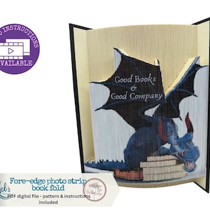 Puede incluir: Un pliegue de libro en forma de dragón azul con el texto "Good Books & Good Company" en las alas. El dragón está sentado sobre una pila de libros. El pliegue de libro está hecho de papel y es un modelo 3D.