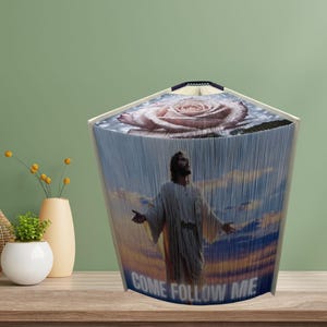 Peut inclure: Une sculpture d'art de livre plié avec une image bleue, rose et blanche d'un homme avec les bras tendus et une rose. Le texte "Come Follow Me" est imprimé au bas de la sculpture.