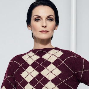 May include: A burgundy and cream argyle pattern knitted dress. The dress features a classic diamond pattern in burgundy and cream colours. The long-sleeved dress is made of a knitted material.