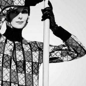 Könnte beinhalten: Schwarz-weißes Bild eines Pullovers mit Rautenmuster, Kapuze und Rollkragen. Die Person trägt schwarze Lederhandschuhe und hält eine weiße Stange. Das Bild ist in Schwarzweiß gehalten.